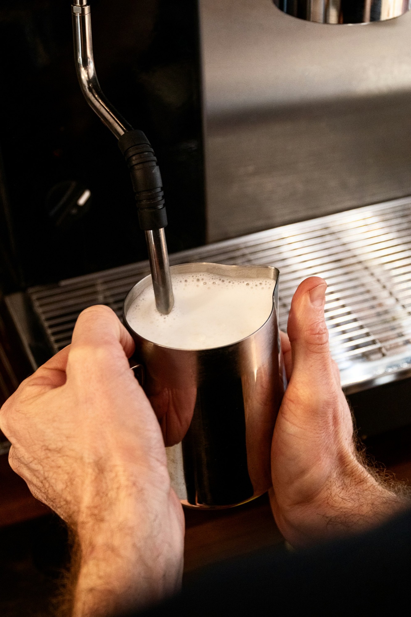 Mani che montano il latte con la lancia a vapore di una macchina da caffè